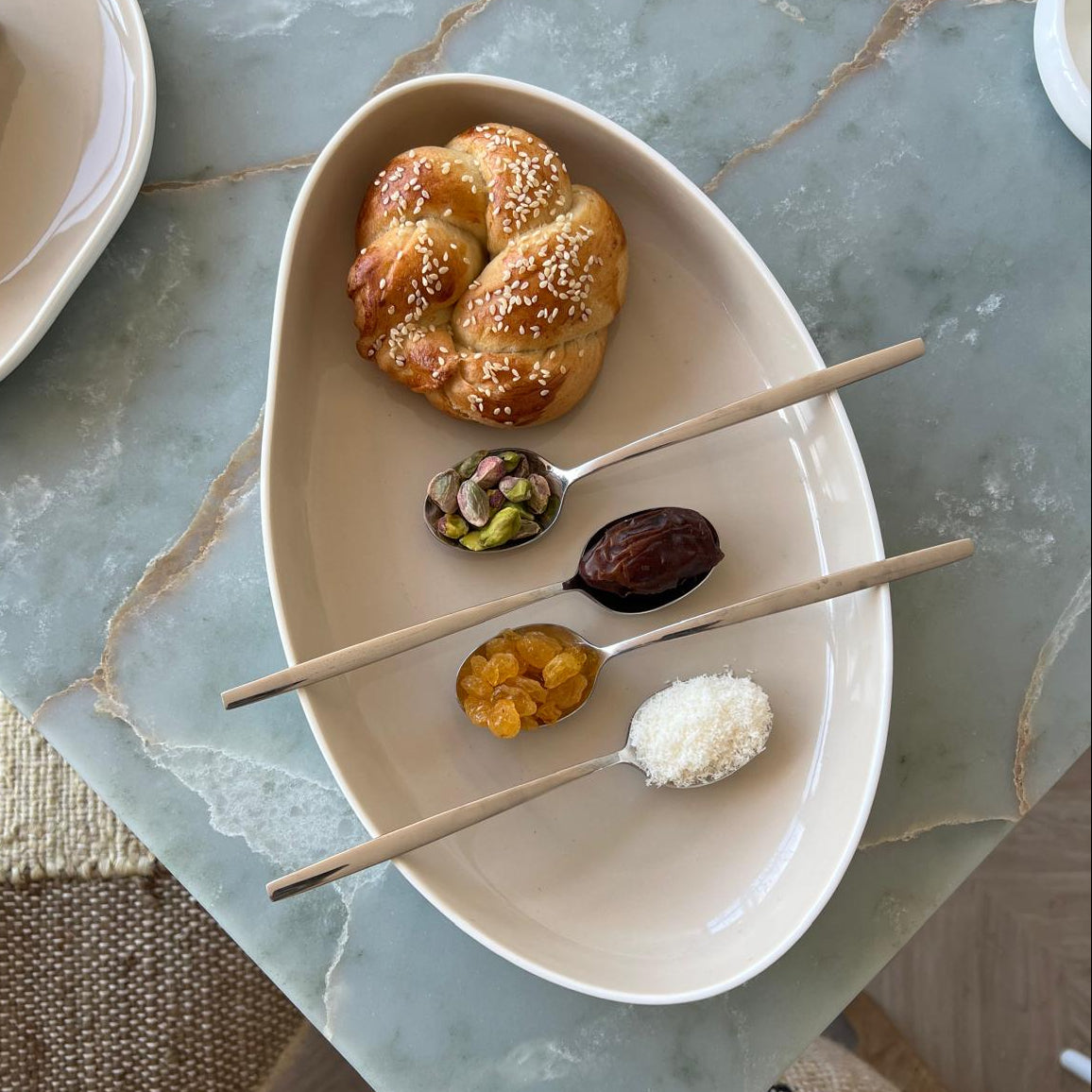 Small plate with Maarouk and three small spoons with dates, coconut, pistachio & raisins on a marble surface.